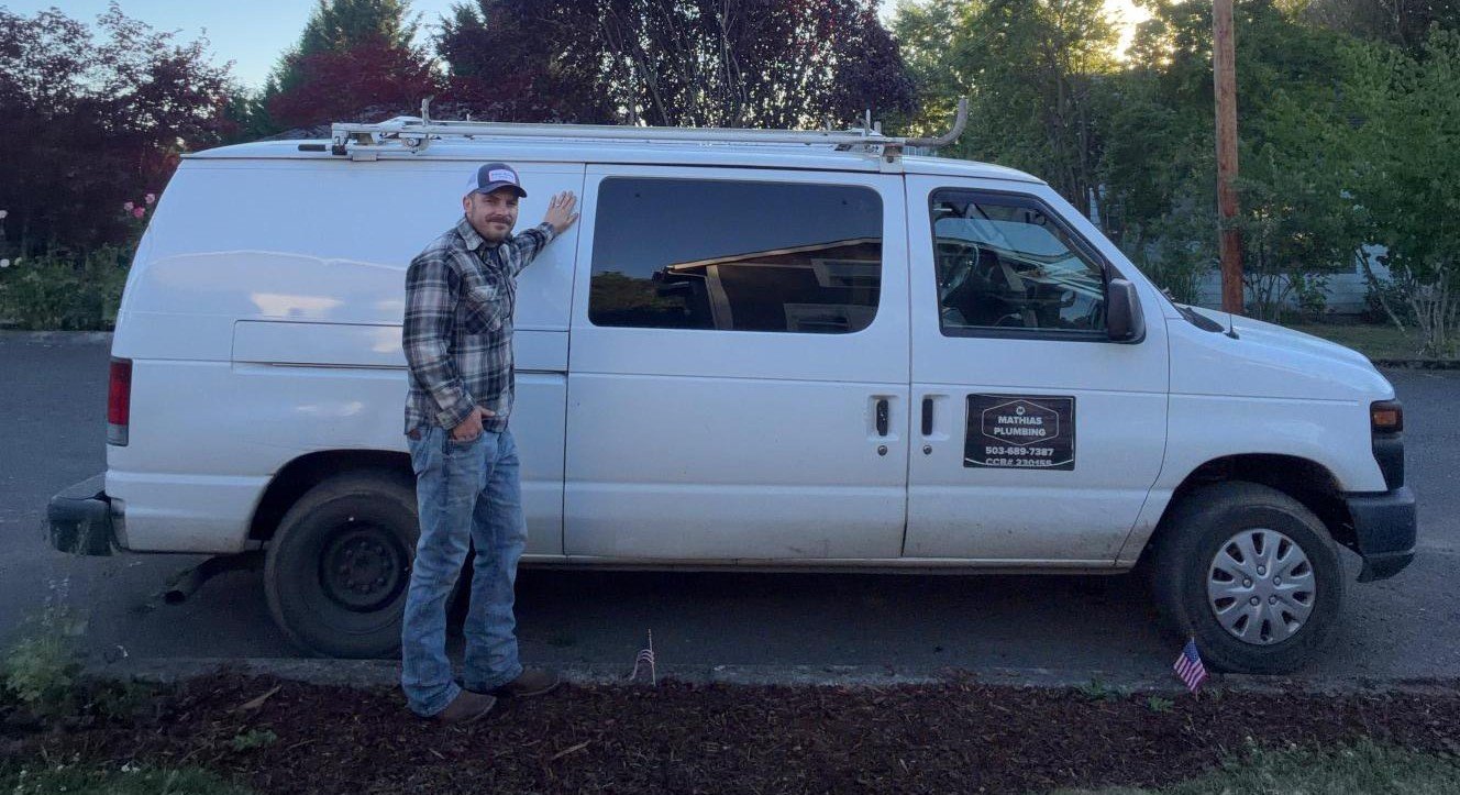 Tannor Mathias, owner of Mathias Plumbing, standing beside his work van in Mount Angel, Oregon